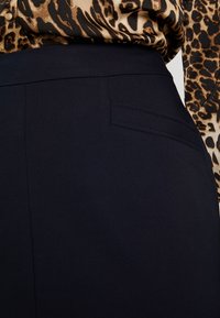 Pantalons ajustés bleu marine avec une texture lisse et une poche arrière unique. Associés à un chemisier à imprimé léopard.