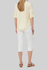 Blouse jaune à manches courtes avec des poignets retroussés, en tissu doux, ourlet arrondi. Associée à un pantalon capri blanc, avec des fentes sur les côtés et des poches arrière.