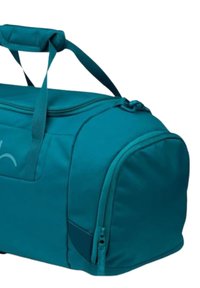 Türkise Sporttasche mit Reißverschluss, kurzen Griffen und einer Seitentasche. Hergestellt aus weichem Stoff mit glatter Textur und minimaler Markenkennzeichnung.