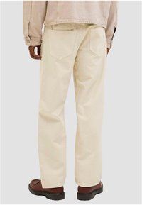 Bež pamučne hlače opuštenog kroja, s dva stražnja džepa i ušivenim detaljima. Uparene s smeđim cipelama s vezicama.