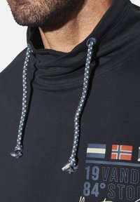 Navy hoodie with a high collar, braided drawstrings, and graphic details including flags and text in contrasting colors. Soft texture visible.