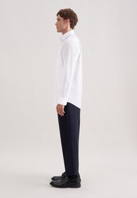 Biała koszula z długim rękawem i kołnierzykiem na guziki, z kieszenią na piersi, zestawiona z ciemnogranatowymi spodniami i czarnymi butami.