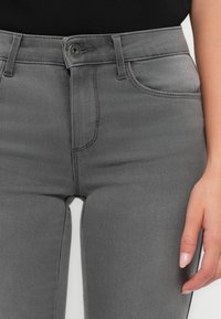 Vaqueros de denim gris de corte ajustado, con cierre de botón clásico, bolsillos frontales y detalles de costura sutiles.