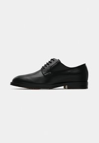 Chaussure Oxford en cuir noir avec une texture lisse, un bout arrondi et six œillets pour les lacets. Présente une semelle plate avec des accents minimalistes.