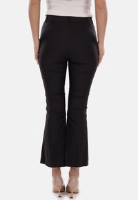 Pantaloni neri a zampa d'elefante realizzati in tessuto morbido, con vita a media altezza e due tasche posteriori. Indossati con tacchi alti beige.