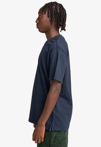 Marineblå bomulds T-shirt med korte ærmer, rund halsudskæring og sideslids i kanten for lettere bevægelse.