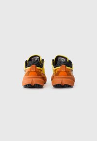 Chaussures de trail running avec une tige en mesh noir ornée d'accents jaunes et oranges, une semelle intermédiaire texturée en orange et une semelle extérieure noire robuste.