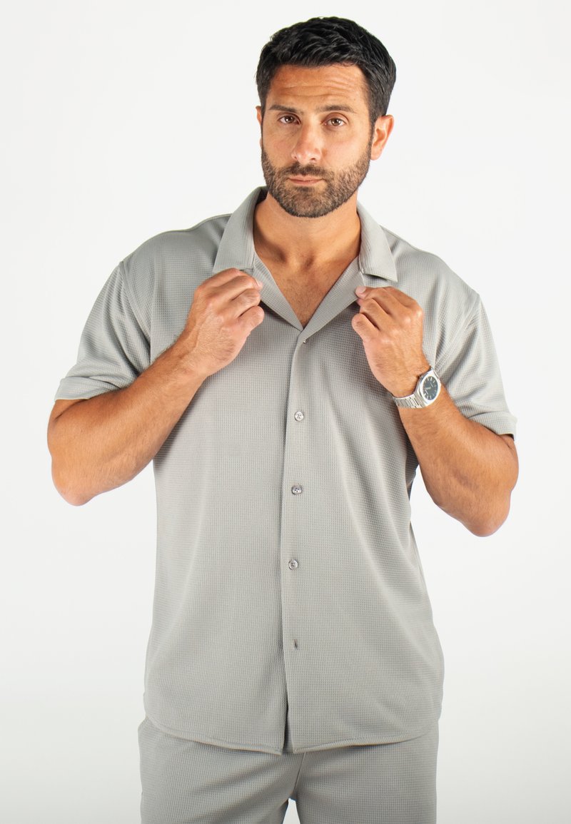 Chemise à manches courtes, col, de couleur gris clair, avec un motif texturé, fermeture à boutons et coupe décontractée.