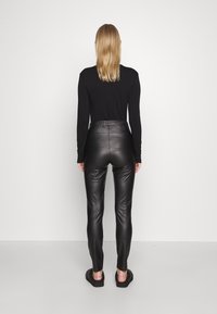 Svarta läderleggings med en slät yta, hög midja och smal passform. Bärs med en långärmad svart topp och mörka skor.