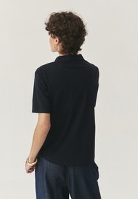 Polo a maniche corte di colore navy, con colletto classico e orlo curvo. Tessuto morbido e dettagli di design minimali per un aspetto semplice.