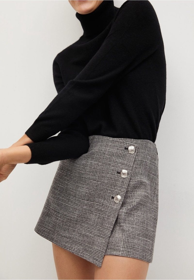 Un col roulé noir associé à une mini-jupe à carreaux grise avec un design enroulé et quatre boutons argentés sur le côté.