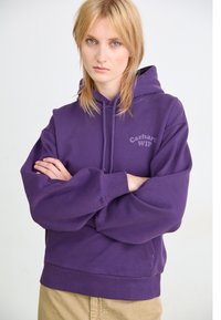 Violetti huppari pehmeästä kankaasta, jossa on etutasku ja ribbireunat. Carhartt WIP -logo painettuna rintaan. Yksinkertainen muotoilu.