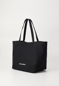 Black tote bag with dual handles, made of textured fabric. Front features a white "KARL LAGERFELD" logo near the base. Simple, rectangular design.