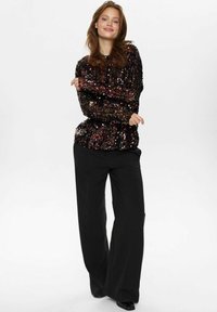 Top nero con paillettes e maniche lunghe, design arricciato, abbinato a pantaloni neri a gamba larga. Tessuto liscio e accenti multicolori vibranti.