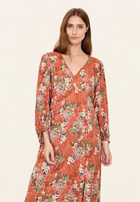 Robe à manches longues, décolleté en V, en orange brique avec un motif floral en vert, blanc et rose. Tissu léger et texturé, design fluide.