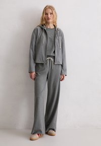 Szara bluza z kapturem i spodnie z miękkiego materiału, z krótkim krojem, ściągaczem, przednią kieszenią i teksturowanym wyglądem, zestawione z beżowymi sneakersami.