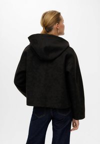 Giacca nera con cappuccio e design corto, realizzata in un tessuto liscio e strutturato. Presenta un motivo sottile e una vestibilità rilassata.