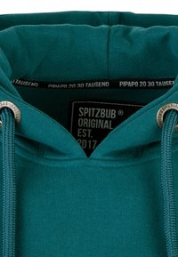Teal hoodie with a drawstring, featuring a soft texture. Includes a label reading "SPITZBUB ORIGINAL EST. 2017" inside the collar.
