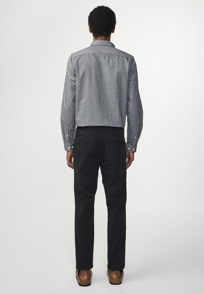 Grå denim skjorte med knapper og lange ærmer, parret med sorte tapered bukser og brune sko, set fra bagen.