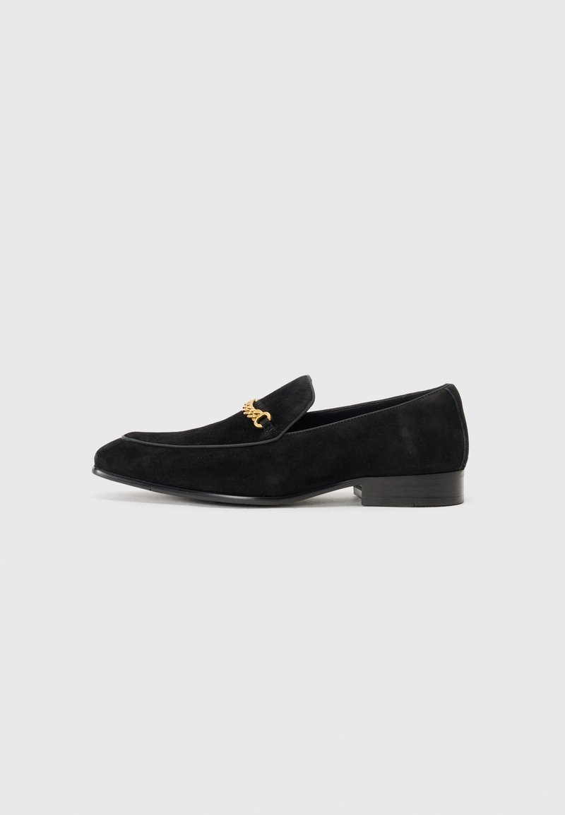 Mocassini in suede nera con tacco basso a blocco, caratterizzati da un'accattivante catena dorata sul davanti e un design elegante con punta affusolata.
