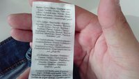 Mão segurando uma etiqueta de vestuário detalhando a composição do tecido: 92% algodão, 6% elastomultiéster, 2% elastano em várias línguas.