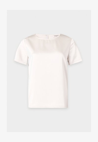 Blouse blanche unie à manches courtes avec encolure ronde, tissu lisse et petite fermeture par bouton au dos du col.