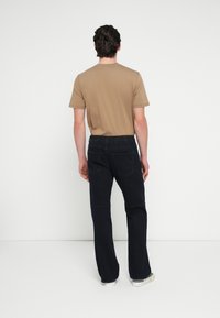 Beżowa koszula z krótkim rękawem, granatowe luźne jeansy z pięcioma kieszeniami, ciemnym szwem i elastycznym pasem, widziane od tyłu.