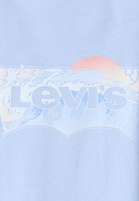 Šviesiai mėlynas medvilninis marškinėliai su dideliu baltu "Levi's" logotipu, kuriame pavaizduota grafika su banga ir saulėlydžiu pastelinėmis spalvomis.