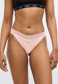 Roze string met kanten randje, zachte stof en een strikdetail in het midden. Zwarte elastische tailleband met merkopdruk.