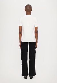 White cotton t-shirt with short sleeves, paired with black cargo pants featuring side pockets and a flared hem. Footwear includes black studded heels.