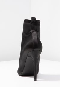 Bottes dcheville en satin noir avec un talon aiguille haut, texture lisse et un soufflet au dos. Caractrises par une coupe ajuste9e et une forme profile9e.