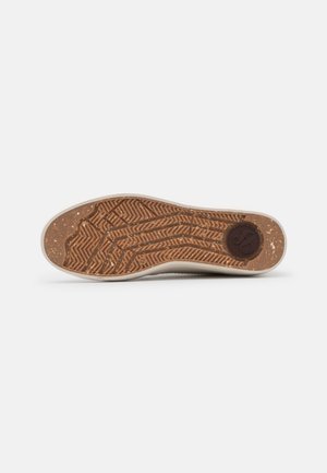 Shoe sole with textured rubber, featuring a zigzag pattern and beige edges, accented with a circular logo in dark brown at the heel.