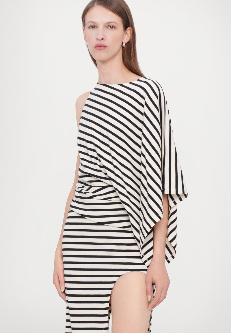 Svartvitrandig klänning med en asymmetrisk design, med draperad ärm och en hög sidofrak för extra detalj.