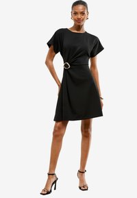 Schwarzes knielanges Kleid mit kurzen Ärmeln, das über ein verdrehtes Taillendesign und eine goldene runde Gürtelschnalle verfügt. Glatte Stoffqualität, lockere Passform.