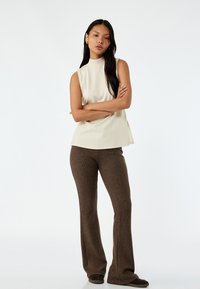 Beige ärmlös topp med hög hals, kombinerad med ribbade, högmidjade bruna utsvängda byxor. Mjuk, texturerad tyg i en neutral färgskala.