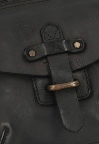 Borsetta in pelle nera con chiusura a pattina e anello metallico con tracolla in pelle. I dettagli delle cuciture sono evidenti e migliorano la sua struttura.