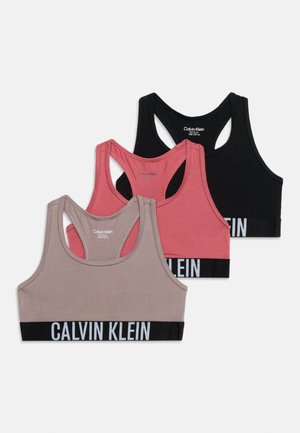 Trois brassières de sport Calvin Klein dos nageur en noir, rose et taupe, chacune avec un élastique noir marqué en blanc en bas.