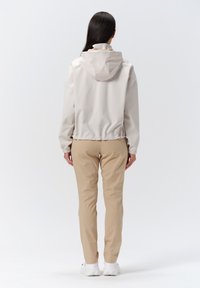 Lys beige vandafvisende jakke med hætte, elastiske manchetter og kant. Parret med tan slim-fit bukser og hvide sneakers.