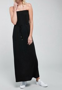 Robe maxi noire sans bretelles avec un corsage froncé, une taille cintrée et une jupe fluide. Associée à des baskets blanches pour un look décontracté.