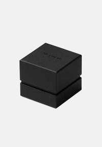 Svart fyrkantig presentask med en strukturerad yta och ett lock. Har präglad märkning på toppen. Enkel, minimalistisk design.