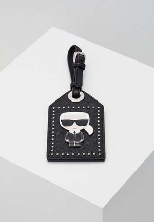Étiquette de porte-clés en cuir noir texturé avec une bordure de clous argentés et un personnage de dessin animé portant des lunettes de soleil et un costume, attachée à une sangle noire avec boucle.