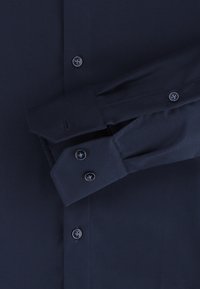 Marineblauwe button-up shirt met een textuurstof. Heeft twee knopen op de manchetten en een enkele knop bij de kraag.