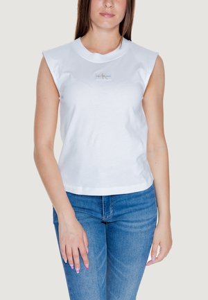 Top bianco in cotone senza maniche con scollo rotondo e un'etichetta del logo al centro, abbinato a jeans in denim blu. Texture liscia, design casual.