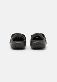 Black slip-on shoes with a rounded shape, made of rubber material, featuring ventilation holes and a textured sole for grip.