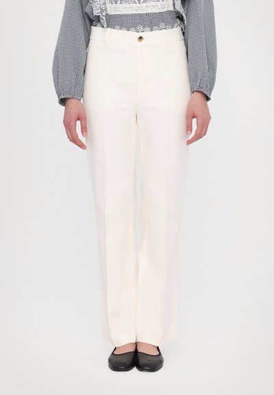 Pantalons larges de couleur crème avec une texture lisse, taille haute, plis et un bouton avant unique. Portés avec des ballerines noires.