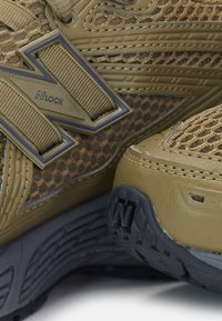 Gros plan de chaussures de course texturées marron et beige avec des panneaux en mesh, un tissu à motifs et des semelles en caoutchouc avec la lettre N.