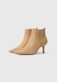 Beige mokkasiininsukat nilkkurit, joissa on terävä kärki, korkea korko ja joustavat sivupaneelit helppoa pukemista varten. Suorapintainen rakenne ja minimalistinen muotoilu.