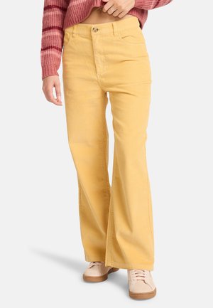 Geel corduroy flared broek met een gestructureerde afwerking, voorzien van voorzakken en een knoopsluiting, gecombineerd met lichte sneakers.