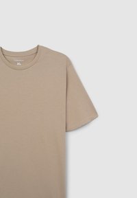 T-shirt in cotone beige con maniche corte, scollatura rotonda e branding minimale sul colletto. Texture liscia, design semplice. Taglia XL.