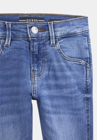 Jean en denim bleu avec un design classique à cinq poches, un léger délavage, des surpiqûres orange contrastantes et une fermeture à bouton en argent.